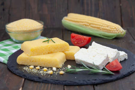 Corn polenta slices on rustic board. Homemade palenta, healthy vegetarian food with cheese and tomato.の写真素材