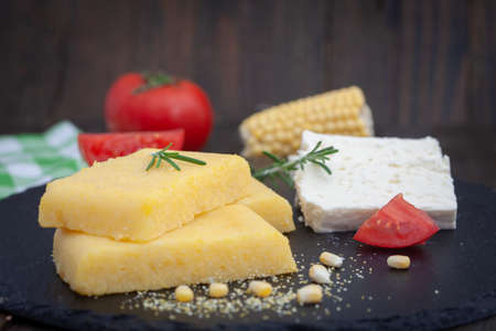 Corn polenta slices on rustic board. Homemade palenta, healthy vegetarian food with cheese and tomato.の写真素材