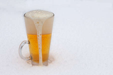 Glass of light beer with foam in the snow. Mug of cold beer during winter.の写真素材