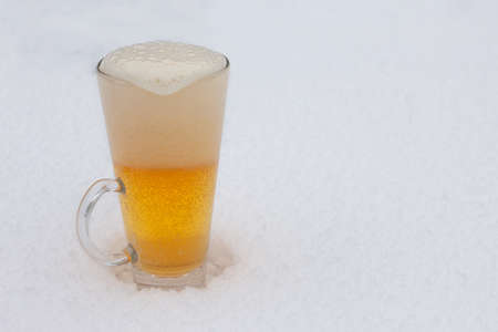 Glass of light beer with foam in the snow. Mug of cold beer during winter.の写真素材