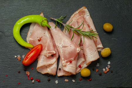 Spicy pork ham slices on black board. Sliced prosciutto with hot chilli, tomato and olives. Top view.の写真素材