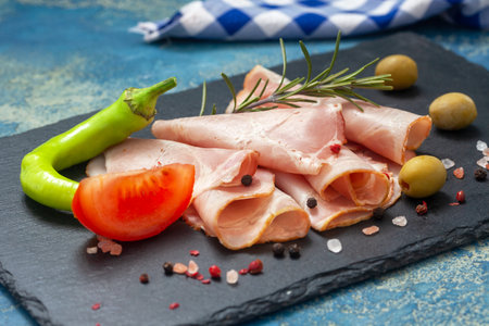 Spicy pork ham slices on black board. Sliced prosciutto with hot chilli, tomato and olives.の写真素材