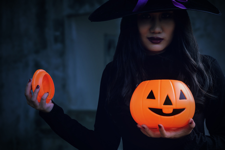 Young woman in witch Halloween costume hold a orange pumpkin over scary dark background.の写真素材