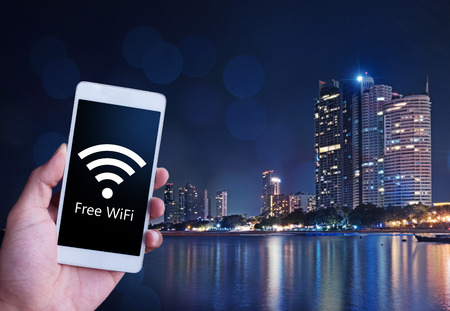 Man is holding a white generic smartphone showing free WiFi. Connecting to public access point on...