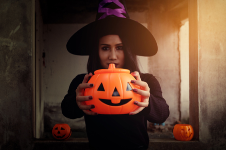 Young woman in witch Halloween costume hold a orange pumpkin over scary dark background.の写真素材