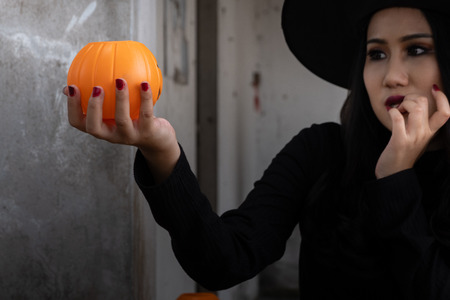 Young woman in witch Halloween costume hold a orange pumpkin over scary dark background.の写真素材