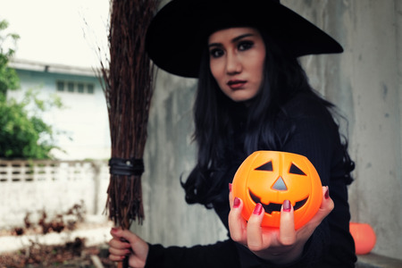 Young woman in witch Halloween costume hold a orange pumpkin over scary dark background.の写真素材