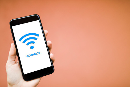 Man is holding a white generic smartphone showing free WiFi. Connecting to public access point.の写真素材