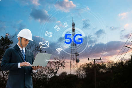 The network engineer is working on the laptop over the 5G network near by antenna tower. Business...