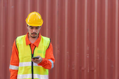 Engineer is working on Smart Phone at container yard. Industrial Container yard for Logistic Import...