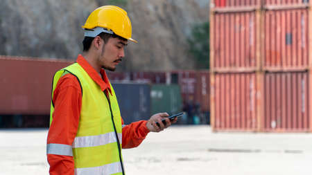 Engineer is working on Smart Phone at container yard. Industrial Container yard for Logistic Import...