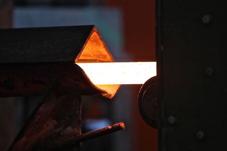 Moving the heated metal rod through the rollers in rolling mill