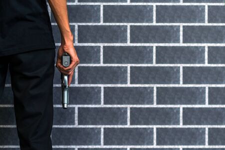 Robber or gangster, thief, Stress man holding gun in hand ready to shoot with grey brick wall Criminal concept.の写真素材