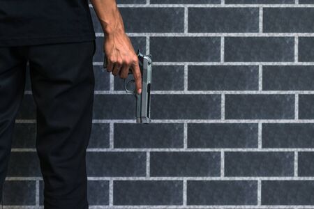 Robber or gangster, thief, Stress man holding gun in hand ready to shoot with grey brick wall Criminal concept.の写真素材
