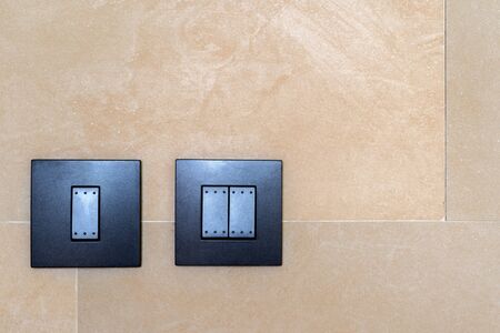 Set of black toggle lighting switches installed on a brown ceramic wall decoration modern building...