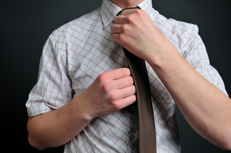 a young man tying his brown tieの写真素材