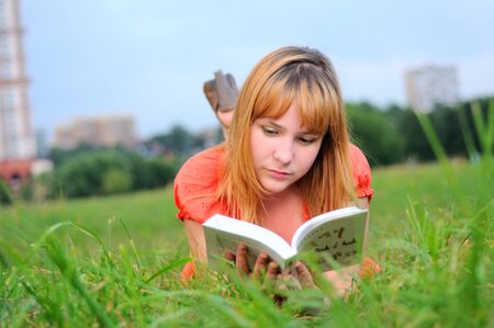 Young woman lying in green field and reading a book.の写真素材