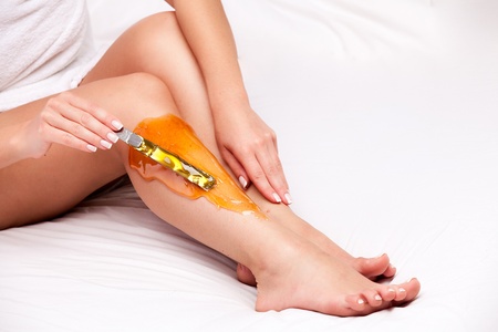 applying wax to females leg to remove hair over white