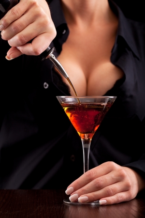 Barmaid stands behind bar mixing drink for clientの写真素材