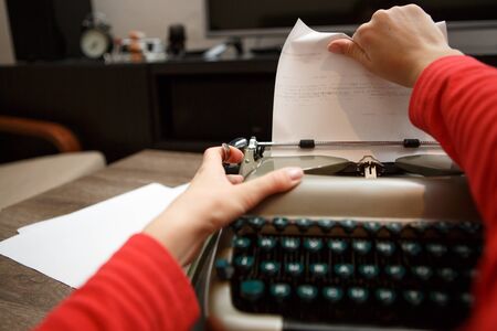 woman working on typewriter pulls paper out at tableの写真素材