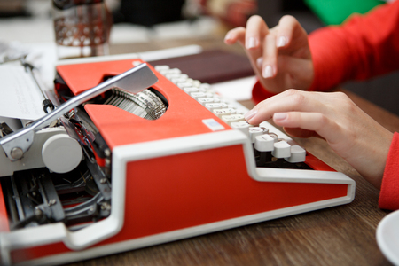woman at table typing on old red typewriterの写真素材