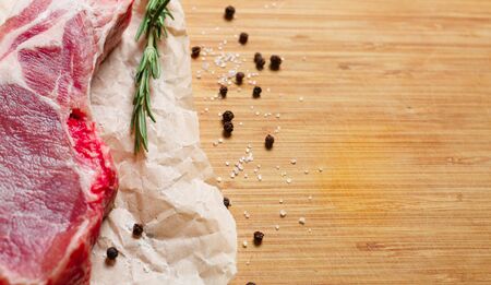 Pieces of crude meat with rosemary and spices on a wooden cutting boardの写真素材