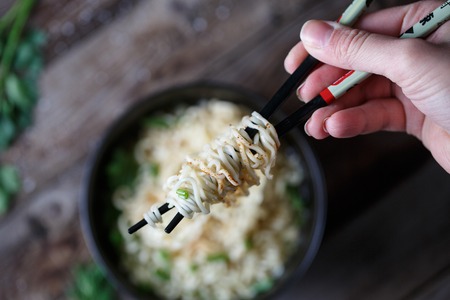 Top view of chinese noodles with fresh peas and chopped green onion on wooden table. Focused on...