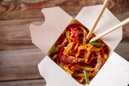 Noodles with pork and vegetables in take-out box on wooden table. Top view.の写真素材