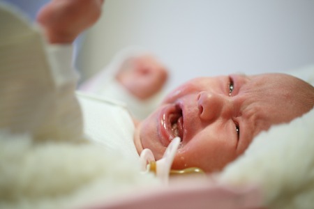 Beautiful newborn baby crying in his bed