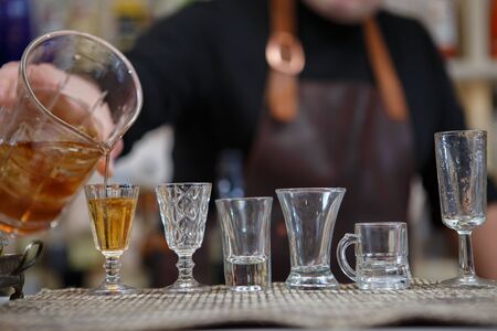 Bartender pours various of alcohol drink into small glasses on barの写真素材