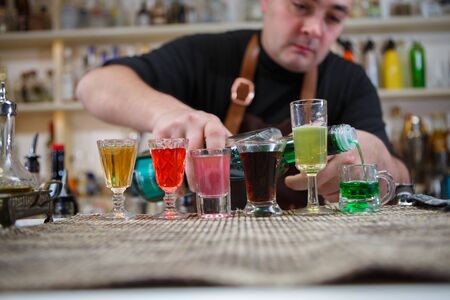 Bartender pours various of alcohol drink into small glasses on barの写真素材