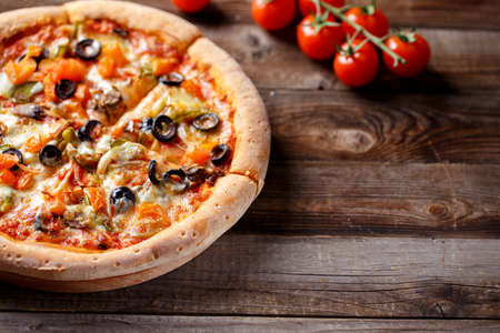 Vegeterian pizza with mushrooms and olives on wooden old table and fresh tomatos, green onion and chilli pepper on backgroundの写真素材