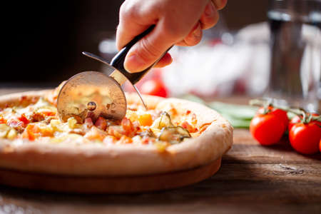 Slicing fresh pizza with pizza knife. Shallow dof. Focused on hand.の写真素材