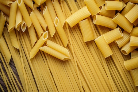 Close up mix of raw dried talian pasta, macaroni, spaghetti, penne on wooden table.  Top view