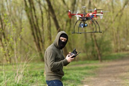 Man in mask operating a drone with remote control. Crime concept