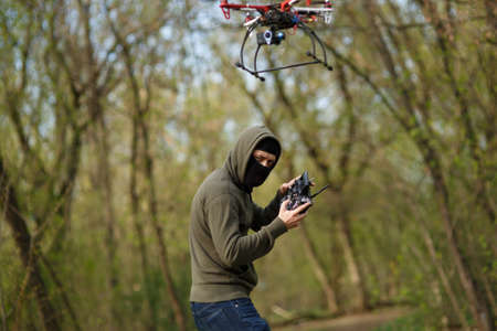 Man in mask operating a drone with remote control. Crime concept