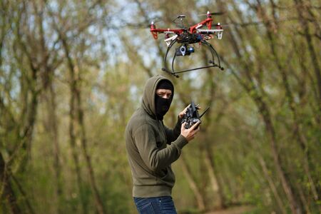Man in mask operating a drone with remote control. Crime concept