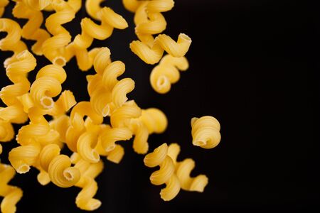 Falling cavatappi pasta. Flying yellow raw macaroni over black background. Shallow dof.の写真素材