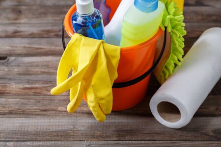 Plastic bucket with cleaning supplies on wood background