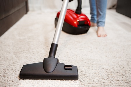 Image of female foot, red vacuum cleaner and black head of vacuum cleaner closeupの写真素材