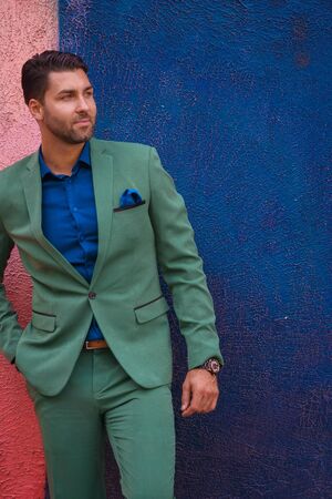 Portrait of young handsome man in green suit against a blue wallの写真素材