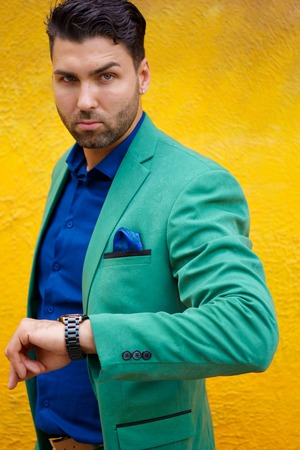 Portrait of stylish young brunette man in green suit on background of yellow wall, vertical image