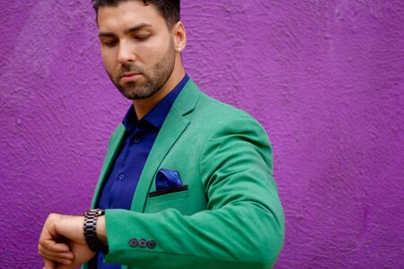 Modern stylish man in green suit watching the time on his watch