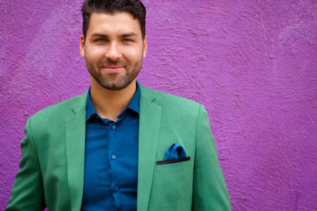 Portrait on purple wall background of fashion smiling brunette man in green suit and blue shirtの写真素材