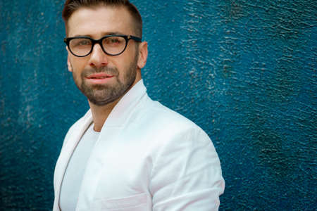Portrait of young handsome stylish man with glasses in white shirt and white jacketの写真素材