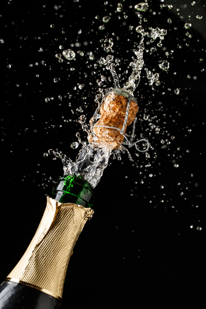 Champagne cork popping and splashing on black background.の写真素材
