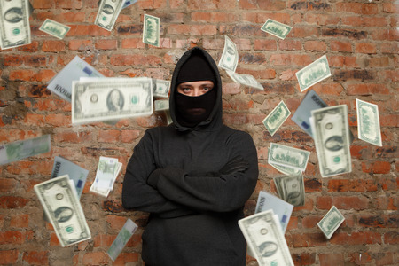 Serious thief near brick wall with flying moneyの写真素材