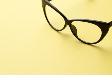 Black glasses with transparent lenses in empty yellow background