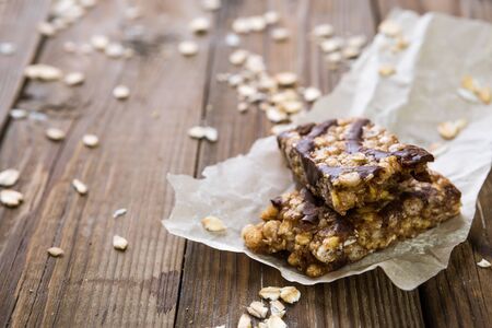 Muesli bars with milk chocolate on paper on wooden tableの写真素材