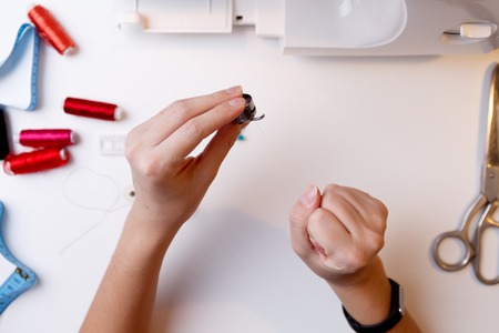 Girl with spool in hands next to sewing machineの写真素材
